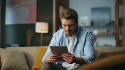 Serious guy working tablet at home. Focused freelancer holding pad sitting sofa