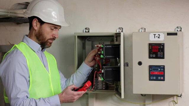 Electrician at work with the tester measures the voltage in the electrical panel of a residential installation. Construction industry protected by helmet