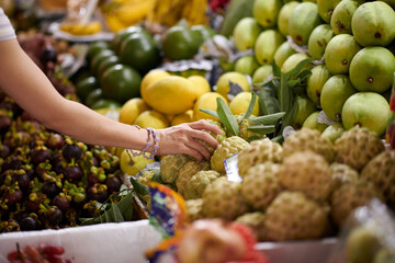 Hand of customer taking custard apple from stall on local market