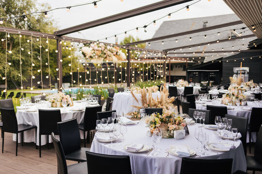 Black chairs and tables decorated white white plates and natural purple and white flowers and reed, candles and gold frames. Wedding decoration and decor, floristic concept