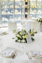  Wedding decorations. Served wedding table with decorative fresh white flowers and candles. Celebration details. flower composition roses plates and candles in candlesticks
