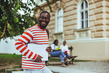 Happy male student standing in front of university building and looking at camera. Copy space. College student portrait, happy man and walking at university