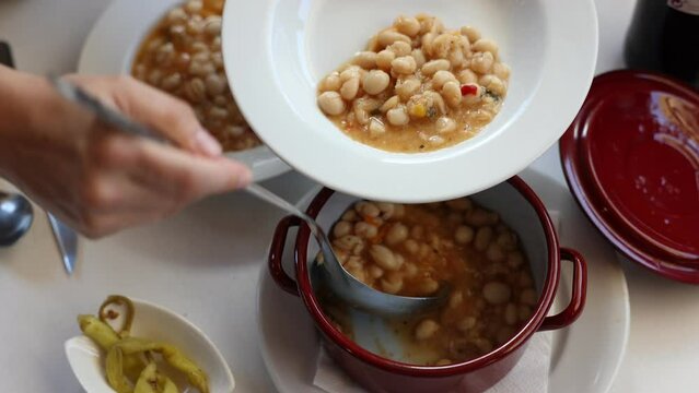 Hearty comfort food with ham hock, vegetables white beans and aromatic herbs. Traditional Spanish meal served with pickled peppers.