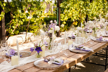 Wedding decorations. Set wedding table with silver plates, purple napkins, decorative fresh and dried flowers, candles and light bulbs. Celebration details, outdoor wedding