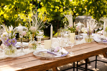 Wedding decorations. Set wedding table with silver plates, purple napkins, decorative fresh and dried flowers, candles and light bulbs. Celebration details, outdoor wedding