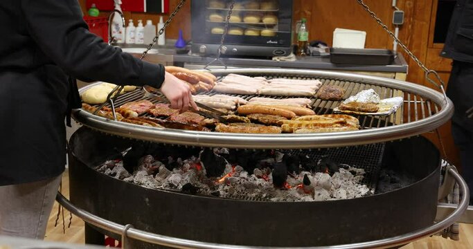 Christmas market in Berlin, Germany. The meat is grilled and roasted over an open fire. Male hands of a chef with a grill tong check the doneness of the meat. Grilled pork and sausage. Street food.