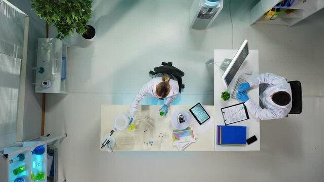 In the frame above is a man and a woman, they are working in a laboratory. The woman is taking a sample of material from a test tube for study. The man is sitting and typing something on a computer