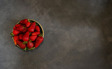 fresh red berries in circular ceramic container top view on gray background with space to fill