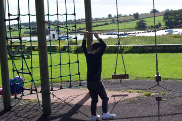 Child boy acrobatics climbing on the equipment. Child playing at the playground in the park on holiday family outdoor activity. 