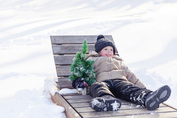 Waiting for summer. Cute little boy lying on a sunbed near Christmas tree in winter and dreaming of summer. Child runs in the winter towards the summer. concept of waiting warm. goodbye winter