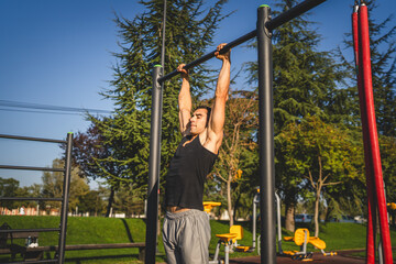 One man muscular male athlete training pull ups outdoor in sunny day