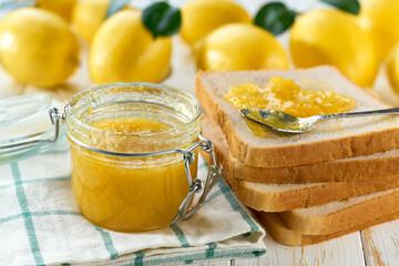 A glass jar of lemon jam on a white wooden table. Homemade lemon marmalade and fresh lemons and green leafs on the kitchen table.