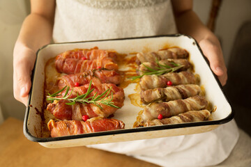 The girl is holding a tray with sausages in bacon