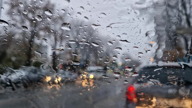 Melted snow and rain drops on the windshield of a car. Blurred outdoor view, winter season sleet as seen out of vehicle window