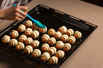 A girl prepares a dish of a pig in a blanket, smears buns with a brush