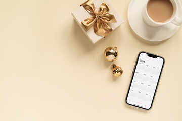 smartphone with 2024 calendar open on it, cup of coffee, gift box and Christmas balls on the table,...