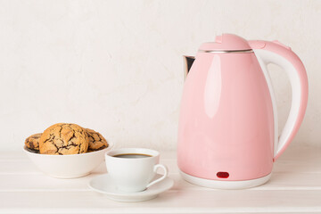Pink electric kettle with cup of tea and dessert on table
