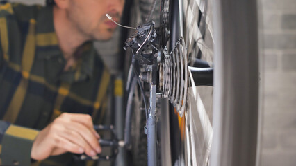 A man pedalling a mountain bike in the workshop. Close-up of a bicycle wheel and transmission. Inspection of a bike by a master, preparing a mtb for the season. - obrazy, fototapety, plakaty