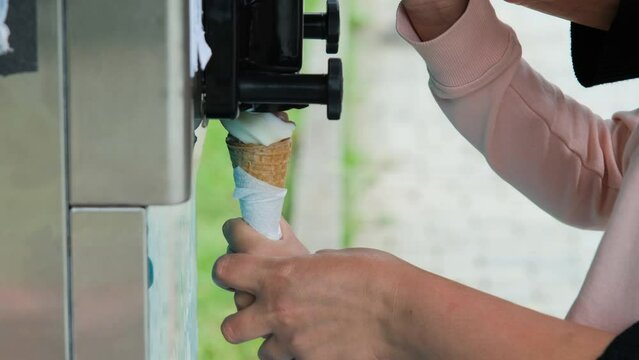 Close-up of seller with help of little girl making ice cream in a waffle cone together outdoors