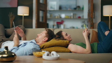 Relaxed pair browsing gadgets sofa. Woman texting telephone guy reading tablet