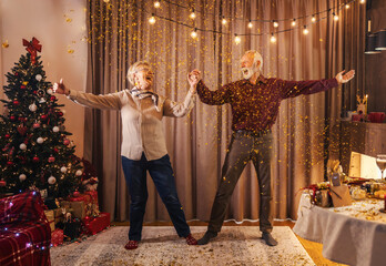 A festive senior couple is dancing at home at christmas and new year's eve with confetti.