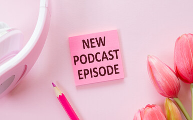 NEW PODCAST EPISODE text on notepad next to headphones, podcasting concept on pink background