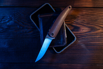 Folding pocket knife and wallet on the table. A sharp knife with a wooden handle. Knife on the table. - obrazy, fototapety, plakaty
