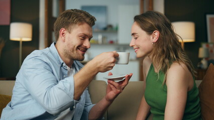 Gentle man treating wife coffee cup at couch closeup. Couple drinking espresso