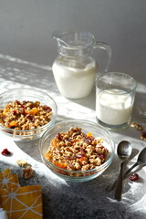 granola with dry fruits, nuts in a transparent bowl, jug and glass with milk, hard light, no people, cozy atmosphere