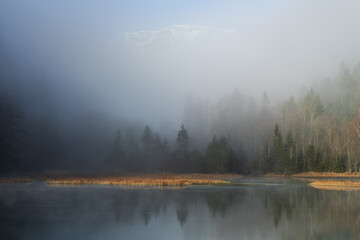 Foggy and misty morning with a mountain lake in Austria in winter with a snowy mountain in the background