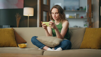 Involved gamer playing cellphone sofa room. Carefree woman enjoying video games