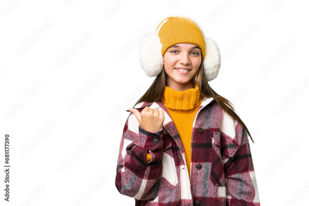 Sticker Teenager caucasian girl wearing winter muffs over isolated background pointing to the side to present a product