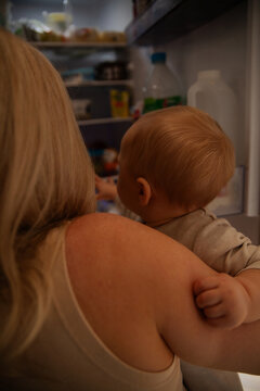 Young mother holding baby with open fridge