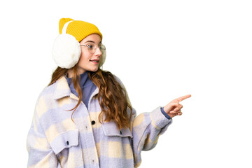 Teenager girl wearing winter muffs over isolated chroma key background pointing finger to the side and presenting a product