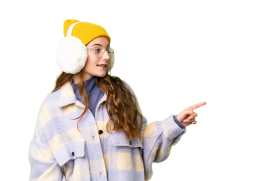 Teenager girl wearing winter muffs over isolated chroma key background pointing finger to the side and presenting a product