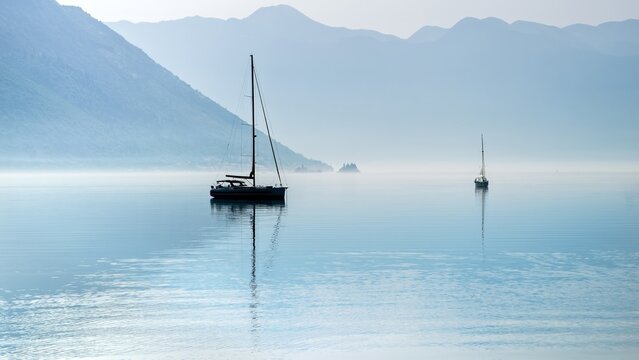 Silhouette of two yachts moored in calm sea harbour with rising morning mist and fog