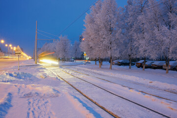 A city street on a winter early morning with snow-covered infrastructure and picturesque frost-covered trees. Twilight.