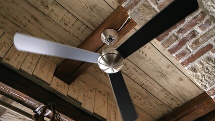 Old ceiling fan lamp spinning in the antique interior with brick walls and wooden roof - obrazy, fototapety, plakaty