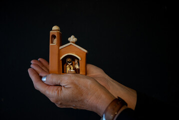 Pesebre en miniatura, con forma de templo, en manos. Navidad