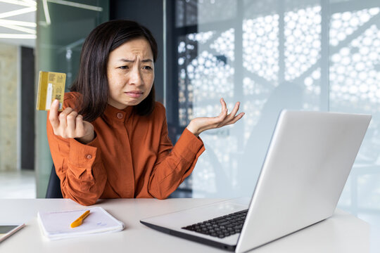 Dissatisfied upset woman sitting at laptop inside office, businesswoman deluded disappointed and sad, holding bank credit card, received funds transfer error, refused online purchase.