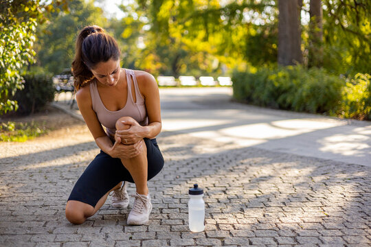Woman runner hold her sports injured knee. Cropped Image of Woman Runner Hold Her Sports Injured Knee Outdoor. Injury From Workout Concept. Pain of Body Part and Bone Broken Theme