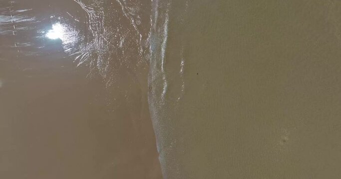 Vertical drone video on the surf line of a sandy beach without people