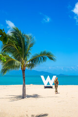 Seascape. A woman walks on a white sand beach near the sea with a palm tree and the letter W. Travel and tourism.