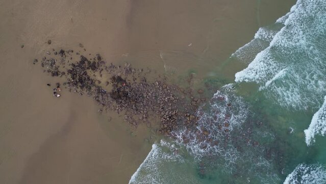 Top-down aerial Slow zoom in surf diagonal right to left Video Drone Footage of Coastal Waves and Boulders