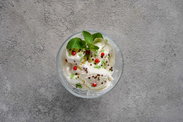 white ice cream in a glass cup decorated with mint leaves and red balls, gray background, minimalism, no people, close-up, top view