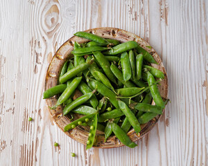 green young peas in pods on a ceramic plate, light wooden background, no people, close-up, top view