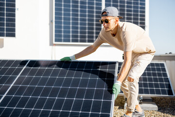 Man installing solar panels on the roof of his house, fitting cell on flat rooftop for self...