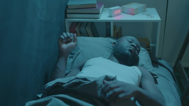 High angle view of Black man lying in his bed and switching sides while having restless sleep during night at home
