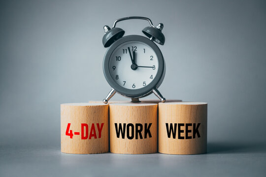Symbol of a 4-day working week. Desk with wooden blocks with the words 4-day work week, alarm clock and beautiful gray background. Copy space. Business concept, change from 5 to 4 day work week