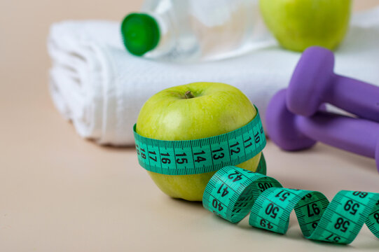 The concept of a healthy image, sports, nutrition, weight loss, fitness. Towel, dumbbells, bottle of water, measuring tape and green apples.